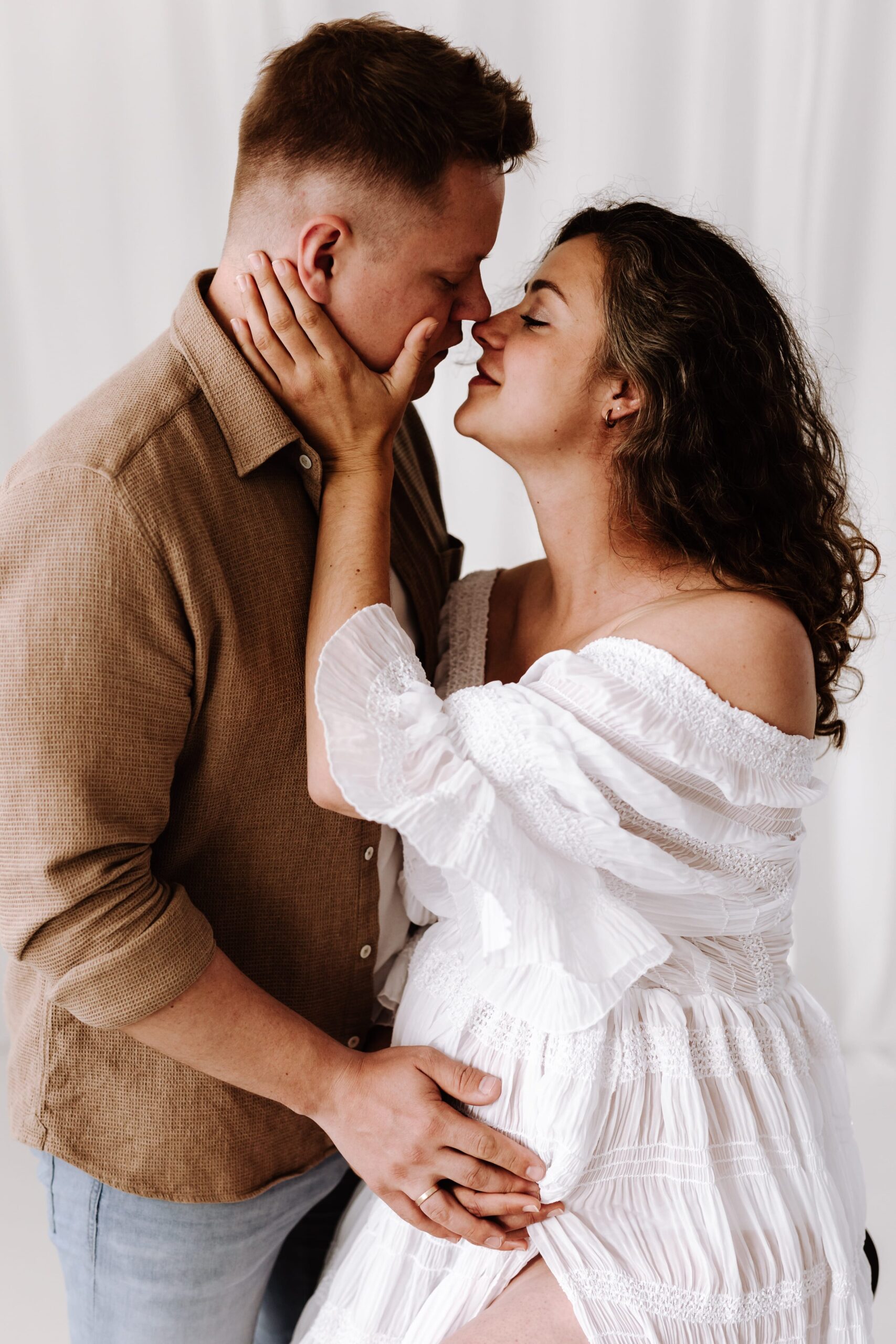 Paar mit Babybauch küsst sich im Studio.